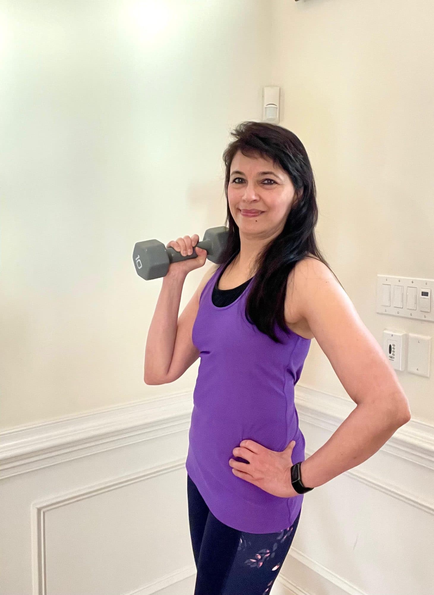 Misha smiling with a dumbbell on her shoulder